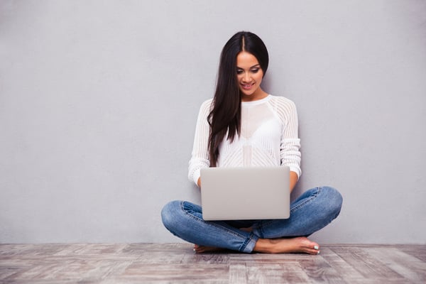 Portrait of a happy casual woman sitting on the floor with laptop on gray background-1