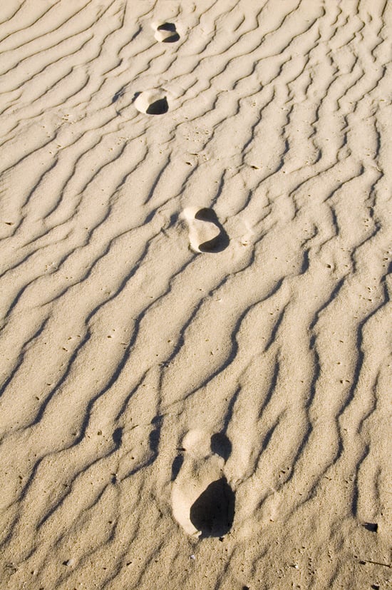 Four human footprints in rippled sand, all heading toward you